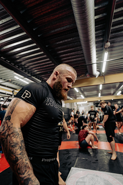 Brazilian Jiu-Jitsu athlete Owen Livesey standing confidently in a training facility, wearing a Progress Jiu-Jitsu rashguard.